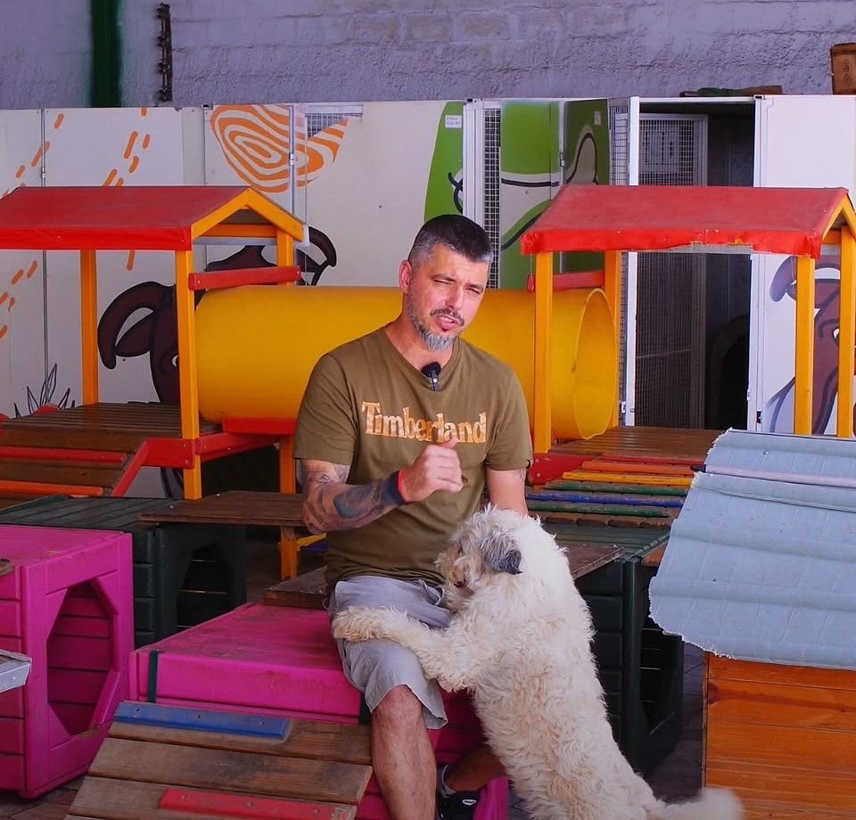 Vanderley sentado no brinquedão da Le Canis, com um cão apoiado nas pernas dele